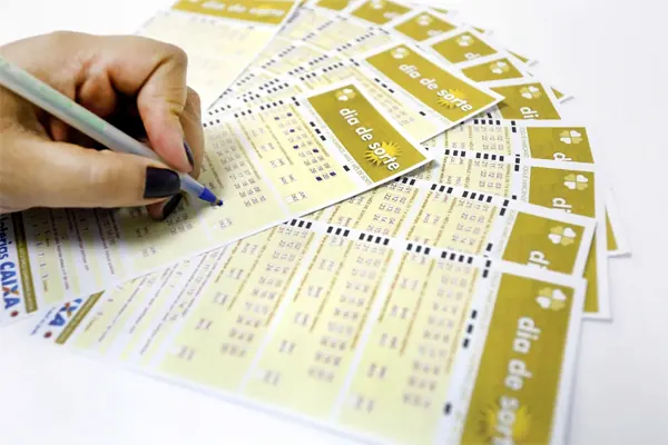 Pessoa preenchendo um bilhete da loteria Dia de Sorte com caneta e vários bilhetes ao redor.