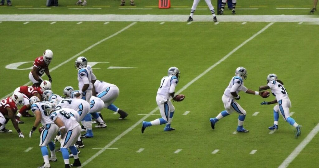 Um running back de futebol americano em ação, correndo com a bola, ilustrando o conceito de "rushing yards" em apostas.