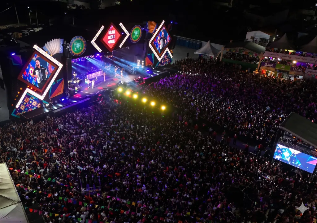 Público celebrando em festa de São João com banners do Esportes da Sorte ao fundo