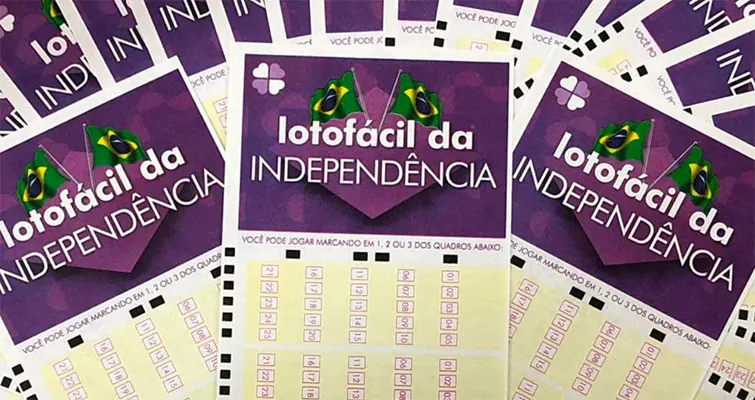 Mãos preenchendo um volante da Lotofácil da Independência com caneta e bilhetes de loteria ao fundo.