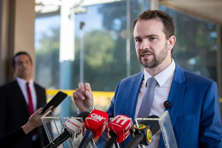 Dario Durigan, Ministro da Fazenda, discursando em um evento, com microfones à frente.